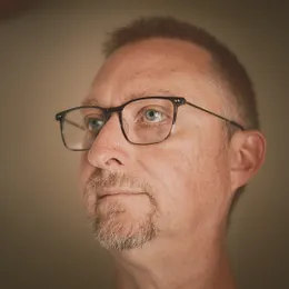 Male adult with short hair and glasses looking upwards against a soft neutral background